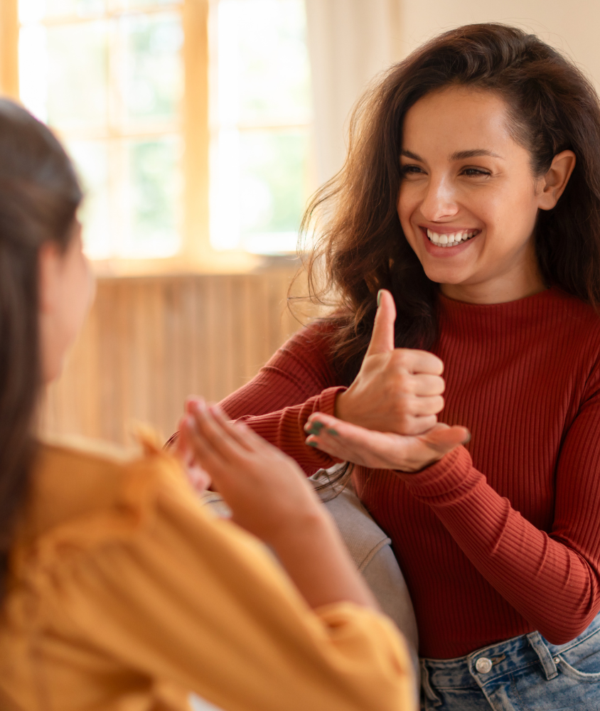 Inicio Mujer sonriendo y hablando en lengua de señas con una niña